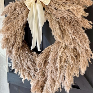 May include: A brown pampas grass wreath with a cream-coloured satin bow. The wreath is hanging on a black door.