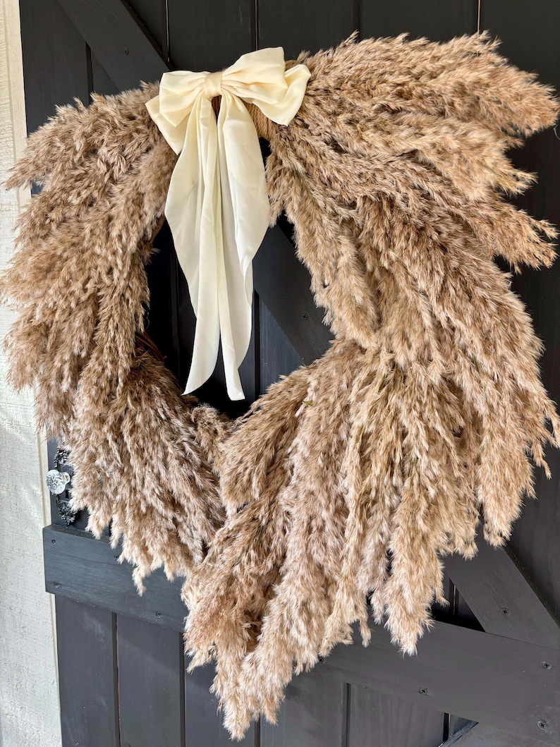 May include: A brown pampas grass wreath with a cream-coloured satin bow. The wreath is hanging on a black door.