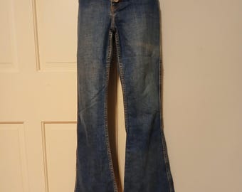 May include: Blue denim flared jeans with a high waist and button closure. The jeans have a classic five-pocket design and a wide, flared leg. The denim has a faded wash for a vintage look.