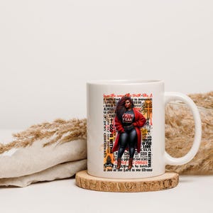 K&ouml;nnte beinhalten: Wei&szlig;e Keramiktasse mit einer schwarzen und roten Illustration einer Frau mit dem Text "Faith Fear" auf ihrem Shirt. Die Tasse hat einen schwarzen Henkel und zeigt eine Vielzahl von inspirierenden Texten in Orange und Schwarz.