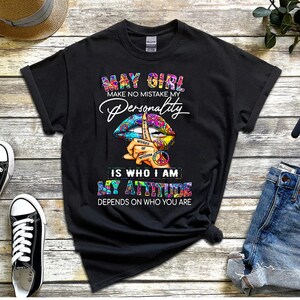 May include: Black t-shirt with a colorful graphic of a peace sign and lips with the text "May Girl Make No Mistake My Personality Is Who I Am My Attitude Depends On Who You Are".