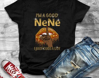 Op de afbeelding: Zwart T-shirt met gouden glittertekst die "I'm a good NeNe I just cuss a lot" zegt. De tekst wordt omringd door een gouden glitterlip met een vinger over de mond.