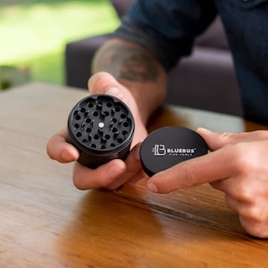 May include: Black metal grinder with a circular design and a removable lid. The lid has the text "Bluebus Fine Tools" printed on it.