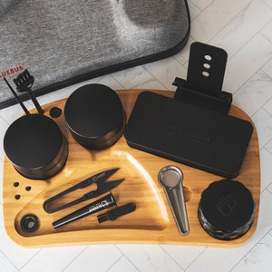 May include: A wooden tray with a black phone stand, a black grinder, a black container, a black spoon, a black and silver pair of scissors, a black brush, and a black and silver tool. The tray has the words "Bluebus" printed on it.