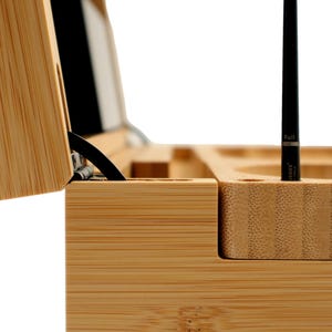 K&ouml;nnte beinhalten: Eine Bambus-Weinpr&auml;sentationsbox, teilweise ge&ouml;ffnet, die eine schwarze Weinflasche und einen schwarzen Stift zeigt. Die Box hat F&auml;cher f&uuml;r Zubeh&ouml;r. Die Holzmaserung ist sichtbar.