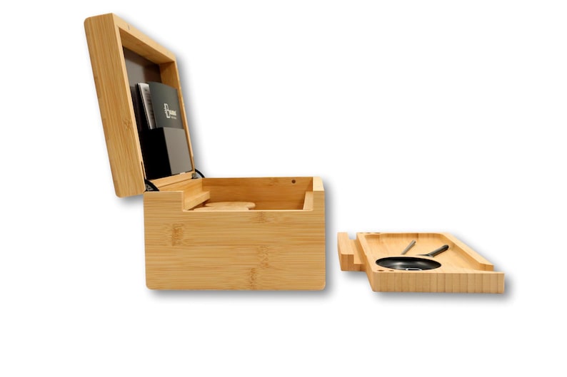 K&ouml;nnte beinhalten: Eine Bambusbox mit Scharnierdeckel, die sich &ouml;ffnet und ein Staufach und einen schwarzen Kartenhalter freigibt. Ein separates Bambustablett mit einer kreisf&ouml;rmigen schwarzen Schale und Werkzeugen befindet sich neben der Box.