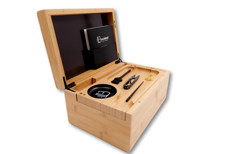 K&ouml;nnte beinhalten: Hellfarbene Bambusbox mit offenem Deckel, die verschiedene Werkzeuge und Zubeh&ouml;rteile zeigt. Die Box enth&auml;lt eine schwarze Sch&uuml;ssel, eine B&uuml;rste, eine Schere, einen Poker und andere Gegenst&auml;nde. Eine schwarze Tasche enth&auml;lt ein Heft.