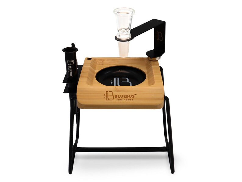 Puede incluir: Un soporte de metal negro con una bandeja de madera y un soporte para bong de vidrio. La bandeja tiene un inserto circular negro con el texto "Bluebus" y "Five Tools" impreso en &eacute;l. El soporte tiene un brazo de metal negro con un soporte para bong de vidrio.