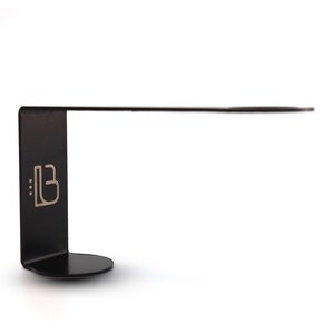 Puede incluir: L&aacute;mpara de escritorio de metal negro con un brazo largo y delgado y una base redonda. La l&aacute;mpara tiene un peque&ntilde;o logotipo en la base que dice "::B".