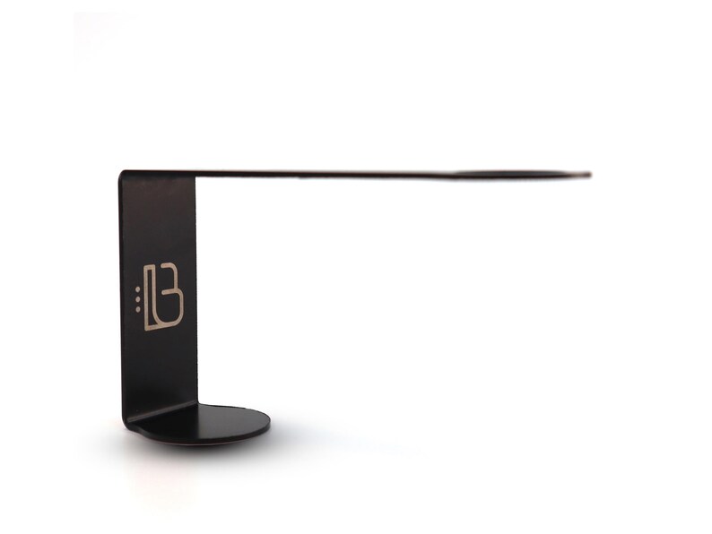 Puede incluir: L&aacute;mpara de escritorio de metal negro con un brazo largo y delgado y una base redonda. La l&aacute;mpara tiene un peque&ntilde;o logotipo en la base que dice "::B".