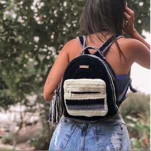 May include: A black and white crocheted backpack with a zipped pocket and a tassel. The backpack has a striped pattern and a black crocheted strap.