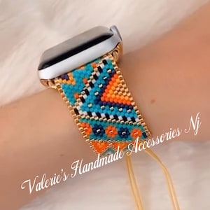 Op de afbeelding: Een kleurrijk kralenhorlogebandje met een geometrisch patroon in tinten blauw, oranje en wit. Het bandje is bevestigd aan een zilveren Apple Watch en heeft gouden accenten. Het bandje heeft twee kwastjes aan het uiteinde. De tekst "Valerie's Handmade Accessories NJ" is zichtbaar in de afbeelding.