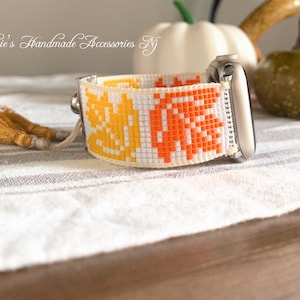 May include: A white, orange, and yellow beaded watch band with tassels. The band is designed with a geometric pattern and fits a smart watch.