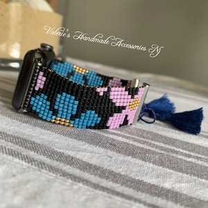 Könnte beinhalten: Ein schwarzes, blaues, pinkfarbenes und goldenes Armband aus Perlen mit einem Blumenmuster. Das Armband ist an einem silbernen Zifferblatt befestigt. Der Text "Valerie's Handmade Accessories NY" ist im Hintergrund sichtbar.