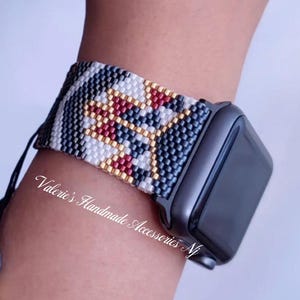 May include: A black, white, gold, and red beaded watch band with a geometric pattern. The band is on a black Apple Watch.