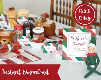 May include: A festive Christmas breakfast scene with pancakes, berries, and toppings. A sign reads "North Pole Breakfast" with 9 days until Christmas. Includes a red and white striped table setting and an elf figurine.