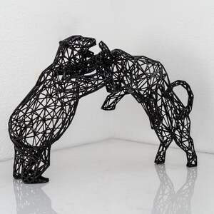 Pode incluir: Uma escultura de arame preto de um touro e um urso frente a frente. A escultura &eacute; feita de arame preto fino e &eacute; muito detalhada. O touro est&aacute; a carregar contra o urso, e o urso est&aacute; a defender-se.
