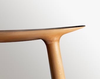May include: Close-up of a light wood table leg with a curved top. The table leg is made of solid wood and has a natural finish.