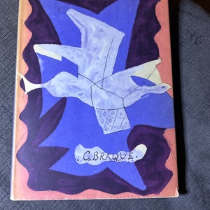 May include: A book cover with a blue and purple abstract painting of a bird in flight. The artist's signature, "G. BRAQUE", is written in black ink at the bottom of the cover.