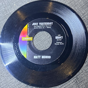 Könnte beinhalten: Schwarze Schallplatte mit weißem Label. Das Label trägt den Text "Just Yesterday" von Matt Monro, die Songwriter, das Plattenlabel und den Produzenten des Songs, George Martin. Die Schallplatte ist eine 45er-Platte.