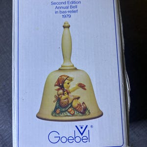 May include: A vintage M.J. Hummel Second Edition Annual Bell in bas-relief from 1979. The bell is cream-colored with a detailed illustration of a child. The box features the Goebel logo and the bell's title.