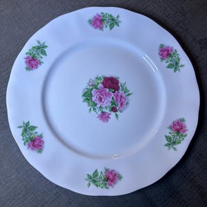 May include: White ceramic dinner plate with a scalloped edge and a floral design featuring pink and red roses with green leaves.