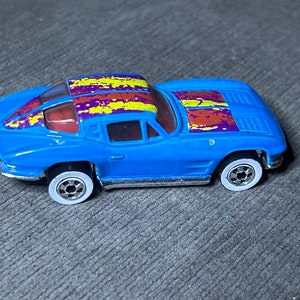 Könnte beinhalten: Ein blaues Spielzeugauto mit weißen Rädern und einer mehrfarbigen Lackierung. Das Auto hat ein gelbes, violettes und rotes Lackdesign auf der Motorhaube und dem Dach.