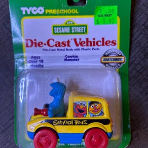 Puede incluir: Un juguete de autobús escolar de metal fundido a presión de Sesame Street con piezas de plástico. El autobús amarillo tiene ruedas rojas y presenta a Monstruo de las Galletas como conductor y a Elmo y Ernie en las ventanas. El embalaje incluye el texto "TYCO PRESCHOOL" y "SESAME STREET".