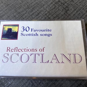 Op de afbeelding: Een cd-hoesje met de titel "30 Favourite Scottish songs" en "Reflections of SCOTLAND" in paarse tekst. De hoes bevat een schilderij van een kasteel in de schemering. De hoes is van doorzichtig plastic.