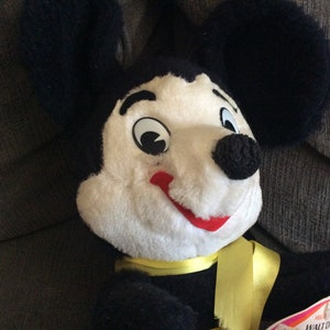 May include: Vintage black and white plush Mickey Mouse toy with a yellow ribbon around its neck. The toy has a red mouth and black button eyes. The tag reads "Walt Disney's Mickey Mouse".