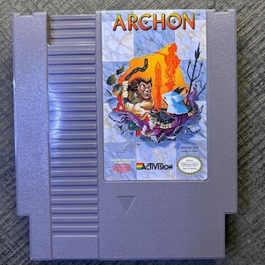 Puede incluir: Un cartucho de juego gris para Nintendo Entertainment System del juego Archon. La etiqueta presenta una ilustración de fantasía de una criatura con cuernos y un caballero en combate, con el título Archon, el logo de Activision y el sello de calidad de Nintendo.