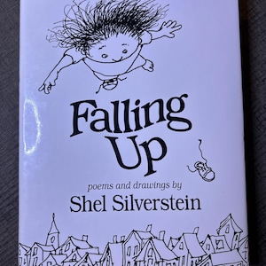 以下が含まれることがあります： 大きな黒い文字で「Falling Up」というタイトルが書かれた白い本の表紙。表紙には、上に向かって浮いている子供の気まぐれなイラストが描かれており、著者のシェル・シルヴァスタインの名前も印刷されています。