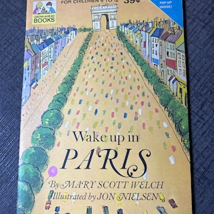 Puede incluir: Un libro desplegable vintage para niños titulado "Wake up in Paris" de Mary Scott Welch, ilustrado por Jon Nielsen. La portada presenta una ilustración colorida de la Torre Eiffel y una escena callejera en París.
