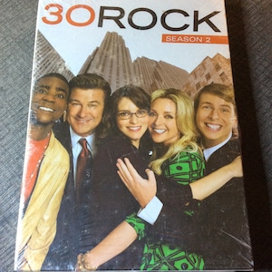 Puede incluir: Caja de DVD de la serie de televisión "30 Rock" con el reparto, incluyendo Alec Baldwin, Tina Fey, Tracy Morgan y Jane Krakowski. La caja es para la temporada 2 de la serie.