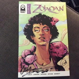 May include: A comic book cover featuring a woman with curly black hair and a pink and purple creature on her shoulder. The comic book is titled "Zojaqan" and is published by Vault Comics. The cover is signed by Kelly Lanzing, Gooden Astone, and Bennett.