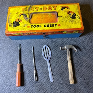 May include: A vintage metal tool chest with a yellow and blue design. The chest has a handle and a label that reads "Busy-Boy Tool Chest". The chest is open and there are four tools inside: a screwdriver, a small screwdriver, a slotted spoon, and a hammer.