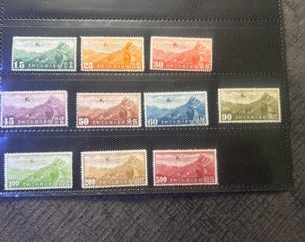 Puede incluir: Una colección de diez sellos postales rectangulares dispuestos en una hoja de presentación de plástico negro. Cada sello presenta una ilustración de un avión sobrevolando un paisaje montañoso con caracteres chinos y valores numéricos del 15 al 500.