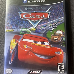 Può includere: Custodia del videogioco Nintendo GameCube per "Cars" di Disney Pixar. La copertina presenta Saetta McQueen, Cricchetto e altre auto da corsa animate su una pista. La custodia ha l'etichetta "Player's Choice" e la classificazione ESRB.