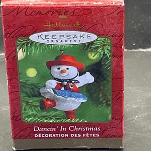 Könnte beinhalten: Hallmark Keepsake-Ornament in einer roten Box. Das Ornament zeigt einen tanzenden Schneemann mit rotem Hut, blauem Rock und roten Stiefeln. Auf der Box steht "Dancin' In Christmas" und "DÉCORATION DES FÊTES".