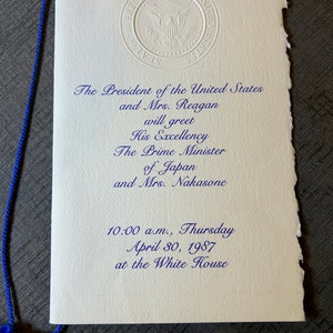 May include: A white invitation card with blue text announcing the President of the United States and Mrs. Reagan will greet His Excellency The Prime Minister of Japan and Mrs. Nakasone at the White House on Thursday, April 30, 1987 at 10:00 a.m.