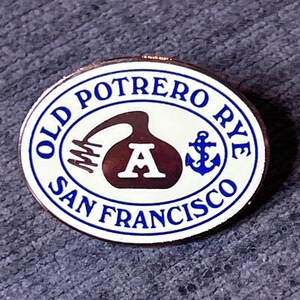 以下が含まれることがあります： 白地と青い縁取りの楕円形のピン。ピンには青色で「OLD POTRERO RYE SAN FRANCISCO」の文字が書かれています。中央には、文字「A」と錨が付いた茶色のボトルの形があります。