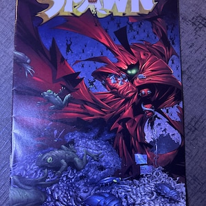 May include: A Spawn comic book issue 122 featuring a character in a red cape with glowing green eyes surrounded by numerous frogs and insects against a dark blue background. The title Spawn is printed in large white letters at the top.