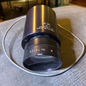 May include: A black zoom lens with the text "ZOOMICON I-CTV 22.5-90 MM F1.5 #6022" and "M.M. S." printed on the side. The lens has a silver ring with the text "NO. 74728" and "S115" printed on it.