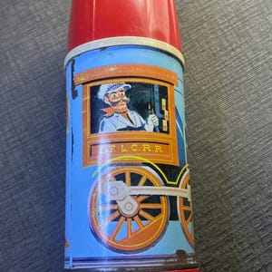 Puede incluir: Termo azul y rojo vintage con diseño de tren. El termo presenta una ilustración de un conductor de tren y el texto "F & C.R.R.". El termo tiene tapa y base rojas, y el cuerpo está decorado con un vagón de tren.