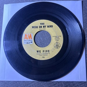 May include: A black vinyl record with a yellow label. The label has the text "AM Records", "You Were On My Mind (Sylvia Fricker)", "We Five", "Produced by Frank Werber for Trident Productions", "770", "M. Witmar & Son (ASCAP)", "Time 2:35 (1136)".