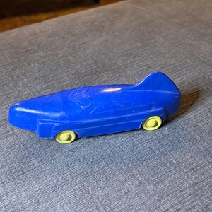 May include: A blue toy car with yellow wheels. The car has a streamlined design and is made of plastic.