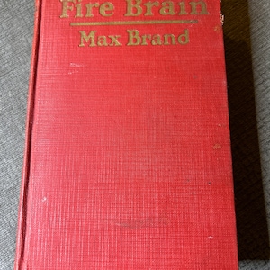May include: A red hardcover book with the title "Fire Brain" and the author "Max Brand" printed in gold lettering.