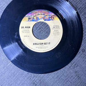 Puede incluir: Un disco de vinilo negro con el texto "DR. HOOK" y "GIRLS CAN GET IT". La etiqueta del disco presenta una imagen colorida y el logotipo de Casablanca Records. El disco es un sencillo de 45 RPM.
