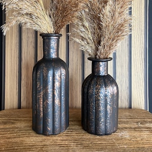 May include: Two black and copper coloured glass vases with a ribbed design. The vases are filled with dried pampas grass.