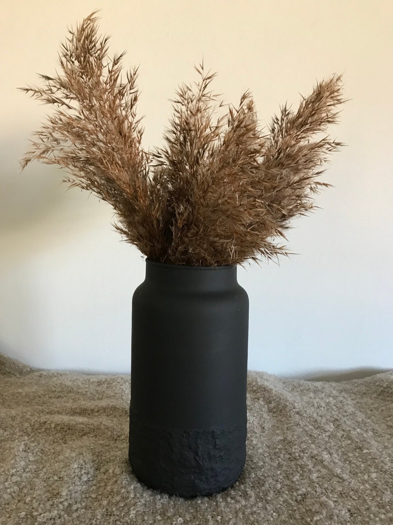May include: A black vase with a textured bottom, filled with dried pampas grass.
